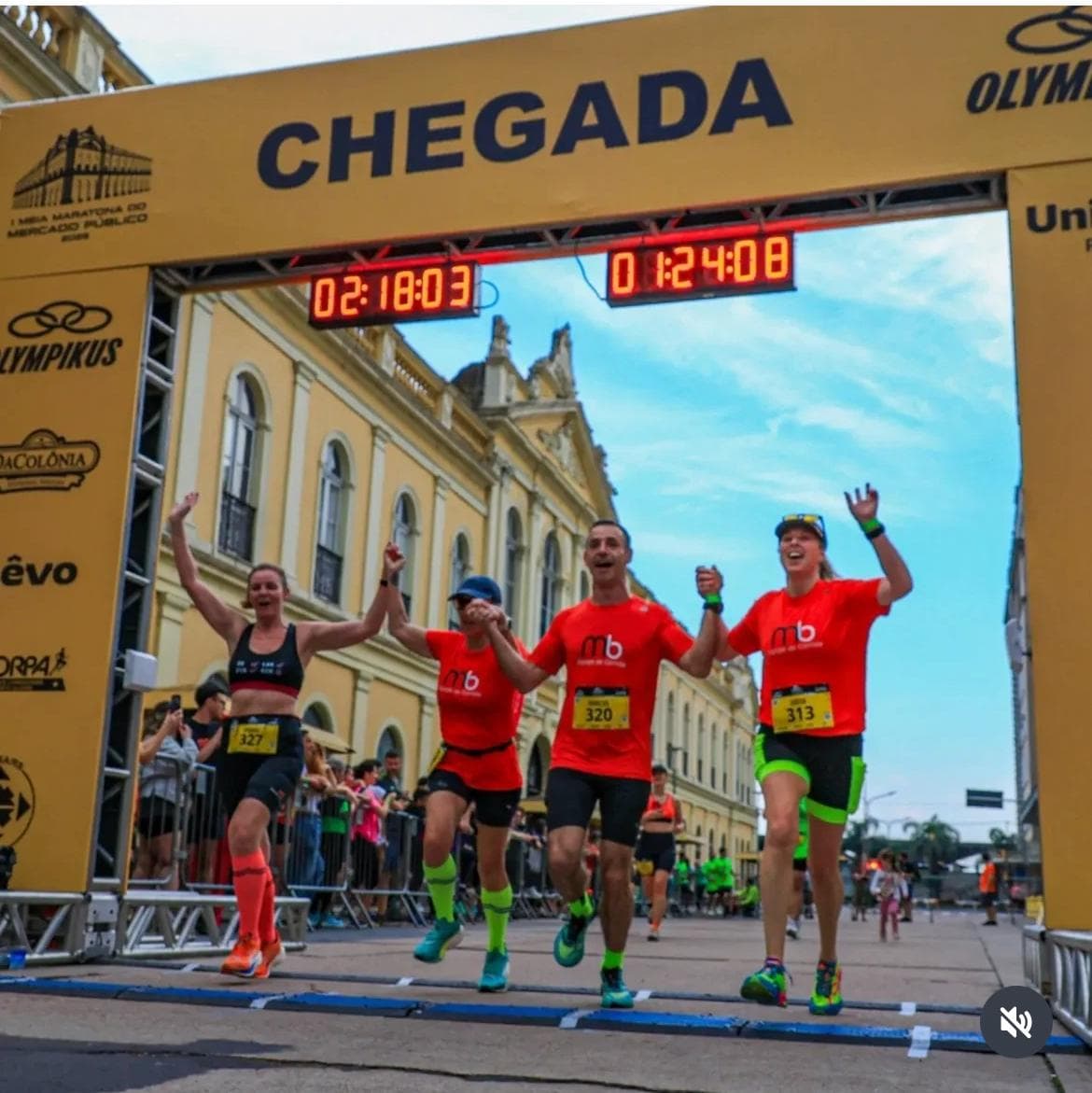 Quatro atletas da equipe cruzando juntos o pórtico de chegada, de braços erguidos.