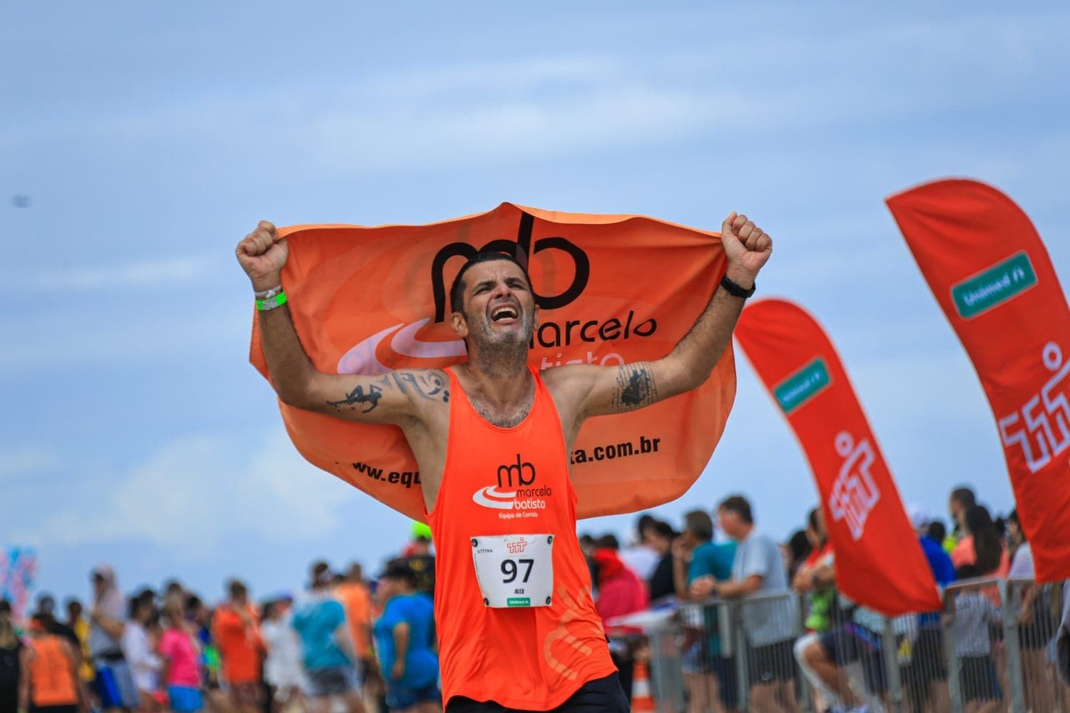 Atleta comemorando a chegada com a bandeira da equipe aberta sobre os ombros.