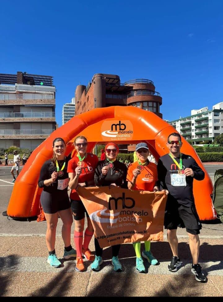 Atletas da equipe posando com as medalhas diante do pórtico inflável laranja.