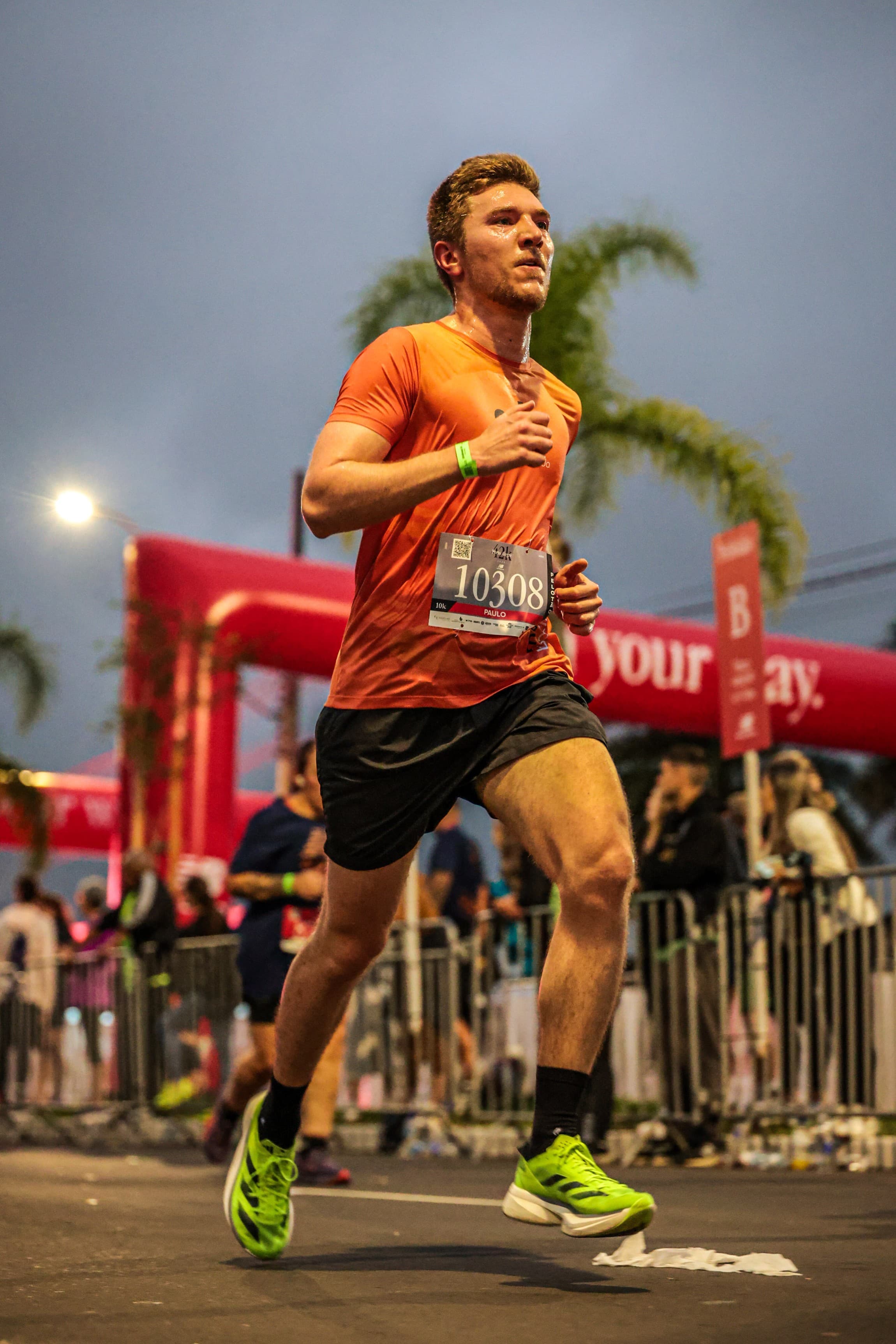 Atleta de camiseta laranja da equipe correndo à noite em prova iluminada.